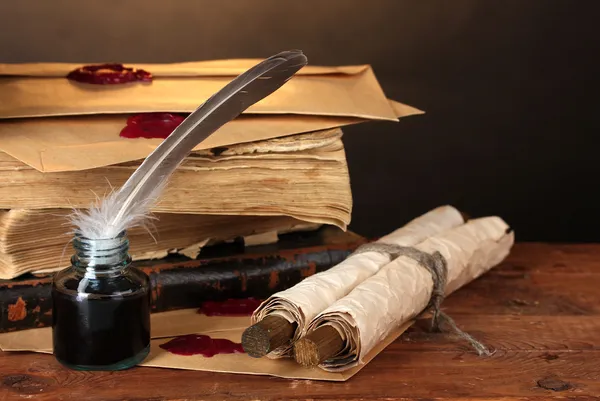 Old books, scrolls, feather pen and inkwell on wooden table on brown background
