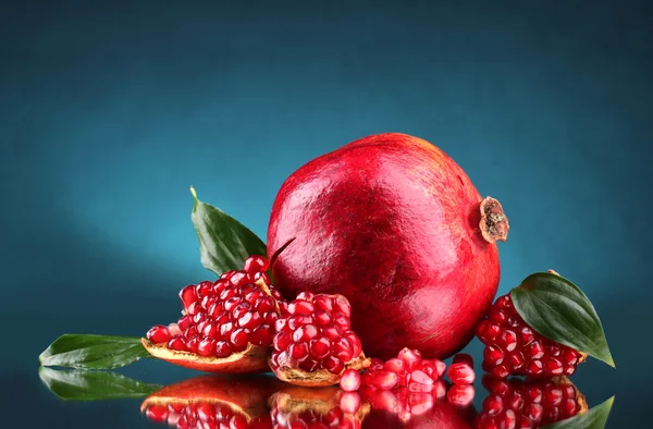 Ripe pomegranate fruit with leaves on blue background