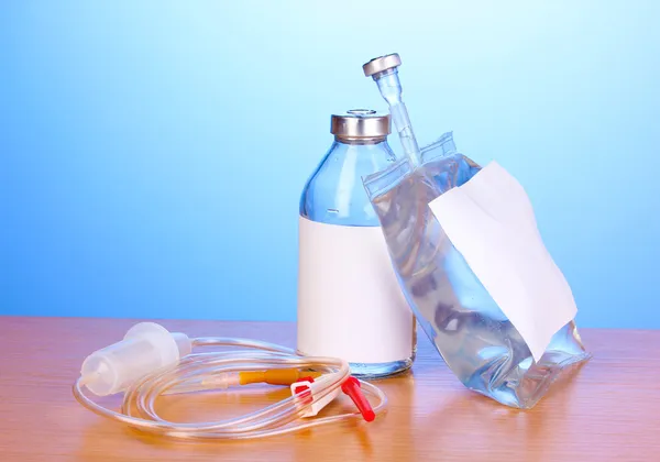 Bottle and bag of intravenous antibiotics and plastic infusion set on wooden table on blue background