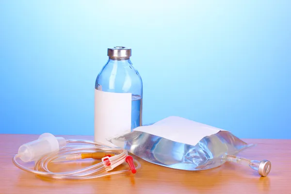 Bottle and bag of intravenous antibiotics and plastic infusion set on wooden table on blue background