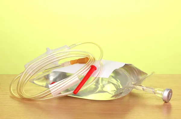 Bag of intravenous antibiotics and plastic infusion set on wooden table on green background