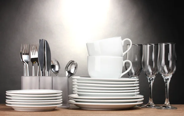 Clean plates, glasses, cups and cutlery on wooden table on grey background