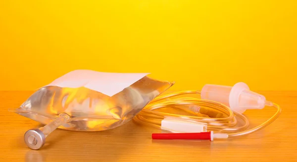 Bag of intravenous antibiotics and plastic infusion set on wooden table on yellow background