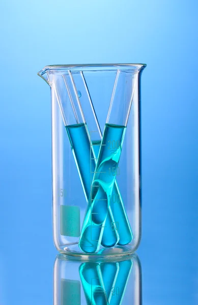 Laboratory tubes with blue liquid in measuring beaker with reflection on blue background