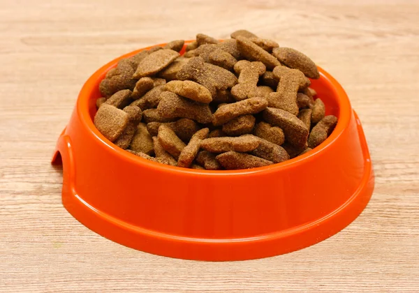 Dry dog food in orange bowl on wooden background