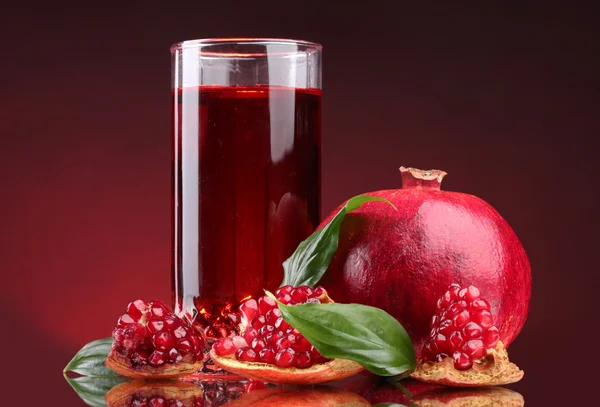 Ripe pomergranate and glass of juice on red background