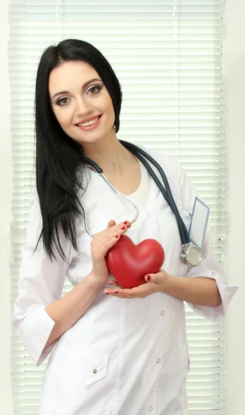 Young beautiful doctor with stethoscope holding heart
