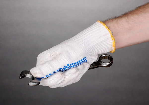Wrench in hand with protection glove on grey background
