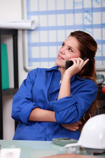 Female worker in blue overalls on the office phone