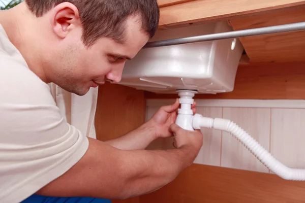Plumber fitting the waste to a kitchen sink