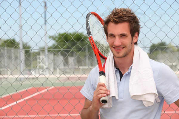 A tennis player posing in front of a tennis court with his racket.