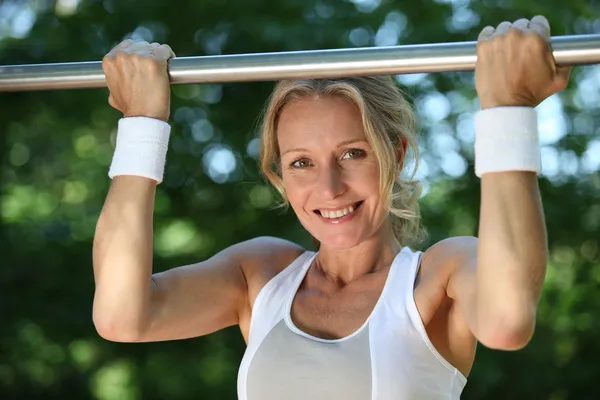 Blond woman exercising on pull-up bar outdoors