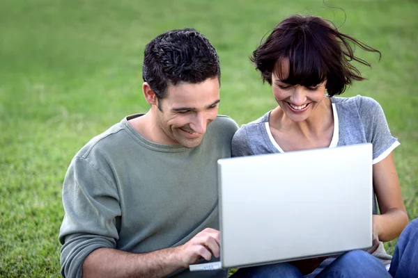 Couple sat with laptop in the park