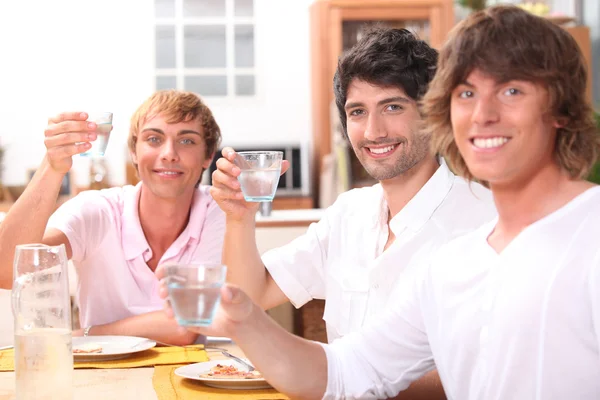 Three young men eating a meal together and drinking water