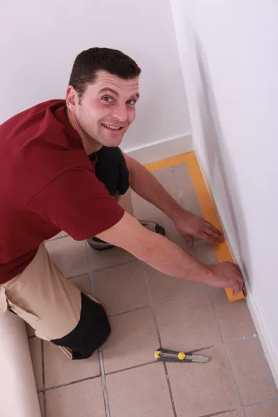 Man putting down tape around the edge of a tiled floor