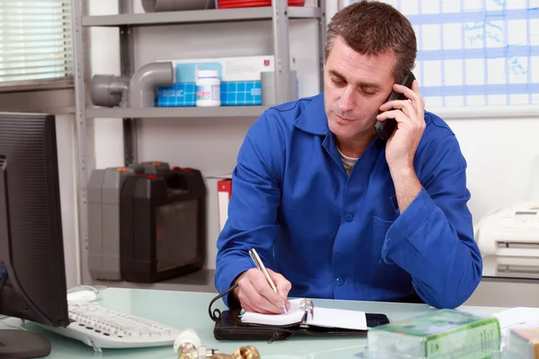 Plumber taking a call in an office and making an appointment in his diary