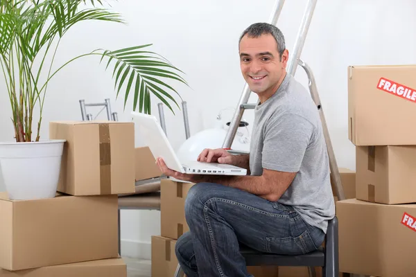 Man using a laptop computer sitting amongst cardboard boxes