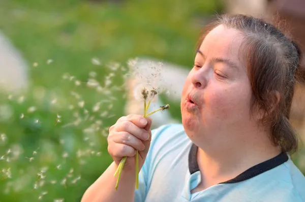 Down syndrome woman blowing dandelion