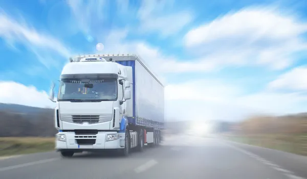 Truck on blurry road over blue cloudy sky background