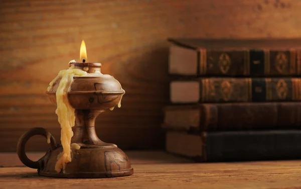 Old candle on a wooden table, old books in the background