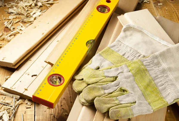 Carpenters level, nails and work gloves are on a wooden planks