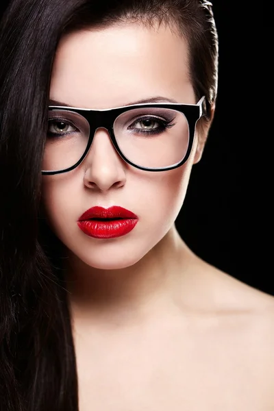 Fashion portrait of beautiful brunette girl model in glasses with birght makeup red lips. Clean skin. Isolated on black