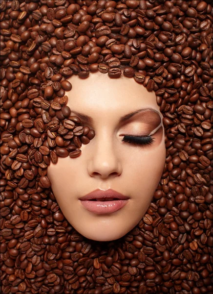 Portrait of a girl\'s face drowned in coffee beans bright brown makeup