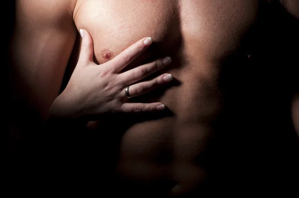 Female hand on the man's muscular chest.