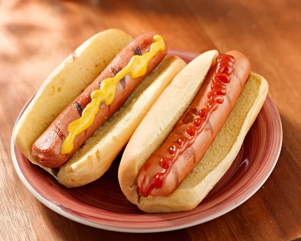 Two hotdogs on a plate with ketchup and mustard.