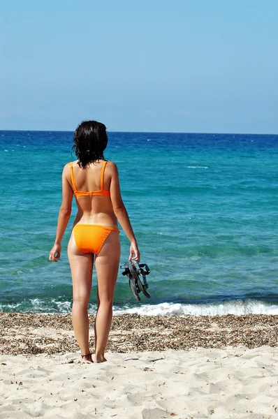 A woman standing in front of the sea in orange bikini and flip-f