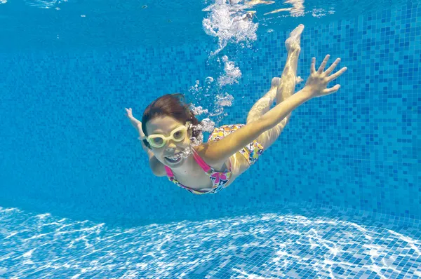 Happy child swims underwater in swimming pool