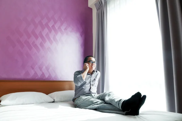 Happy young man talking on mobile phone in bedroom