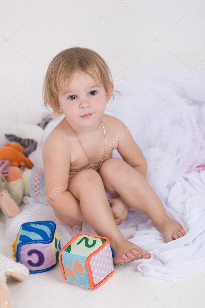 Little naked girl is seating with her toys