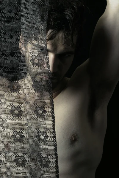 Portrait of beautiful young shirtless man behind black lace