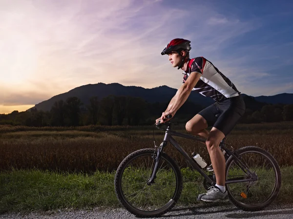 Young man training on mountain bike at sunset