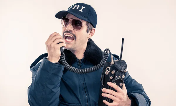 FBI agent in blue riot jacket talking loudly on vintage radio