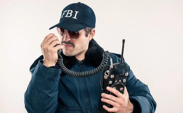 Young white FBI officer in blue jacket talking on vintage radio