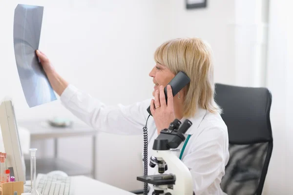 :Middle age doctor woman speaking phone and looking on patients roentgen