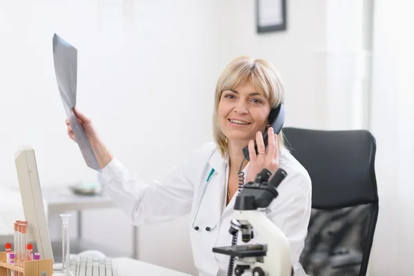 Middle age doctor woman holding patients roentgen and speaking phone