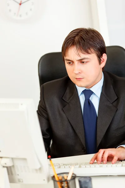 Concentrated modern businessman sitting at office desk and working on compu