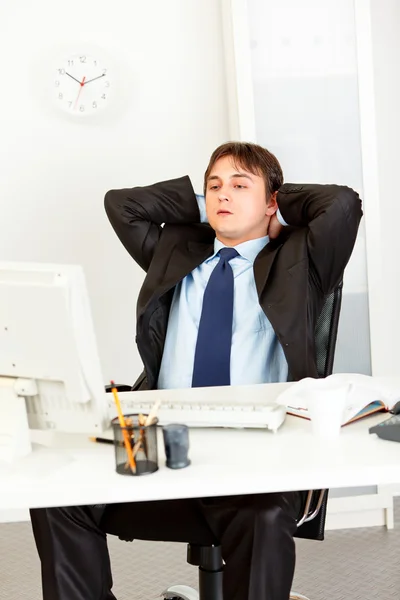 Tired businessman sitting at office desk and looking at computer monitor.