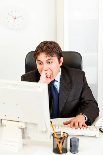 Stressful businessman sitting at office desk and looking at computer monito