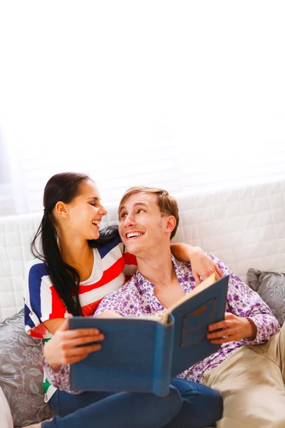 Laughing young couple sitting on couch and looking in photo albu