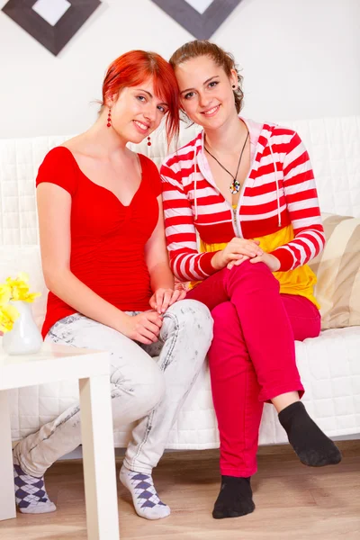 Two happy girlfriends sitting on sofa at living room