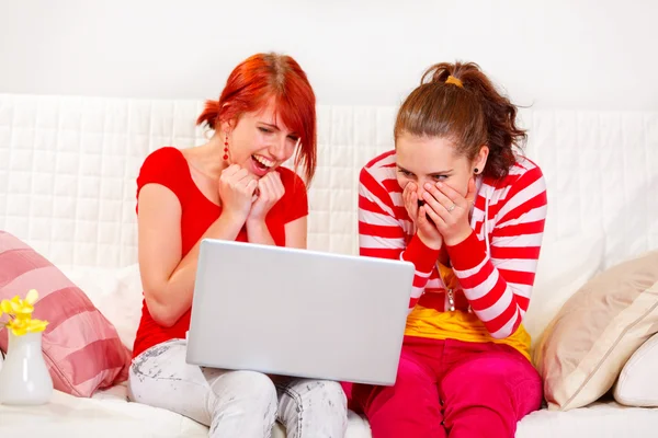 Laughing girlfriends looking on laptop