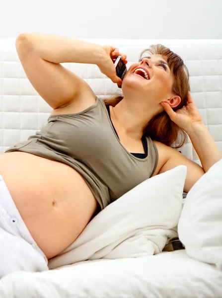 Laughing beautiful pregnant woman relaxing on sofa and talking mobile phon