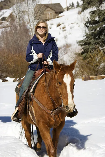 Woman horseback riding in snow.