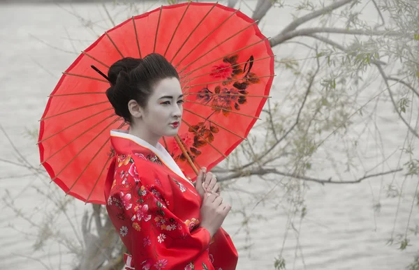 Geisha with red umbrella at the riverside
