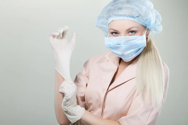 Young nurse in medical gloves and hospital mask on a white background.