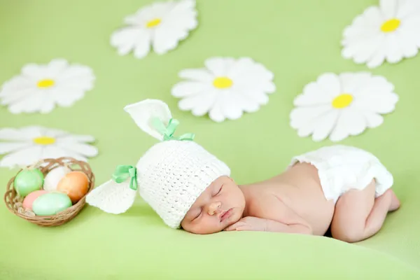 Sleeping baby infant with a rabbit ears and carrot among daisy